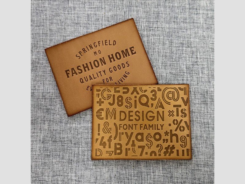 Two tan leather patches with engraved lettering on gray fabric