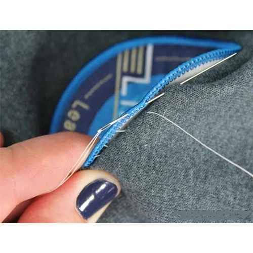Needle and thread sewing a blue-edged patch onto grey fabric