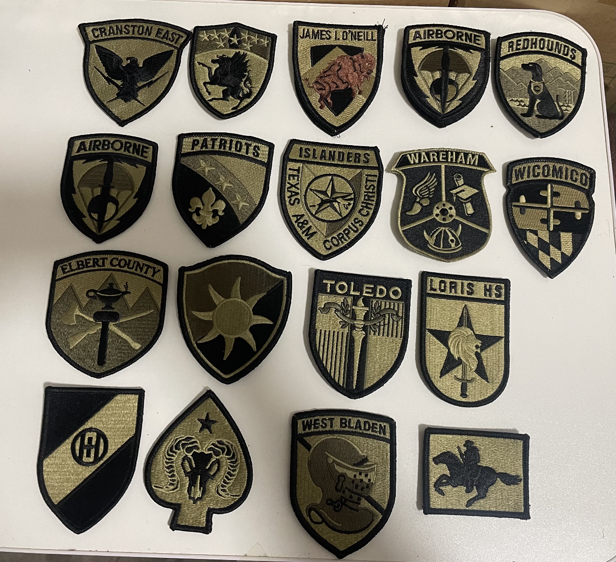 Custom military patches with olive and black embroidered shield designs arranged on a white board