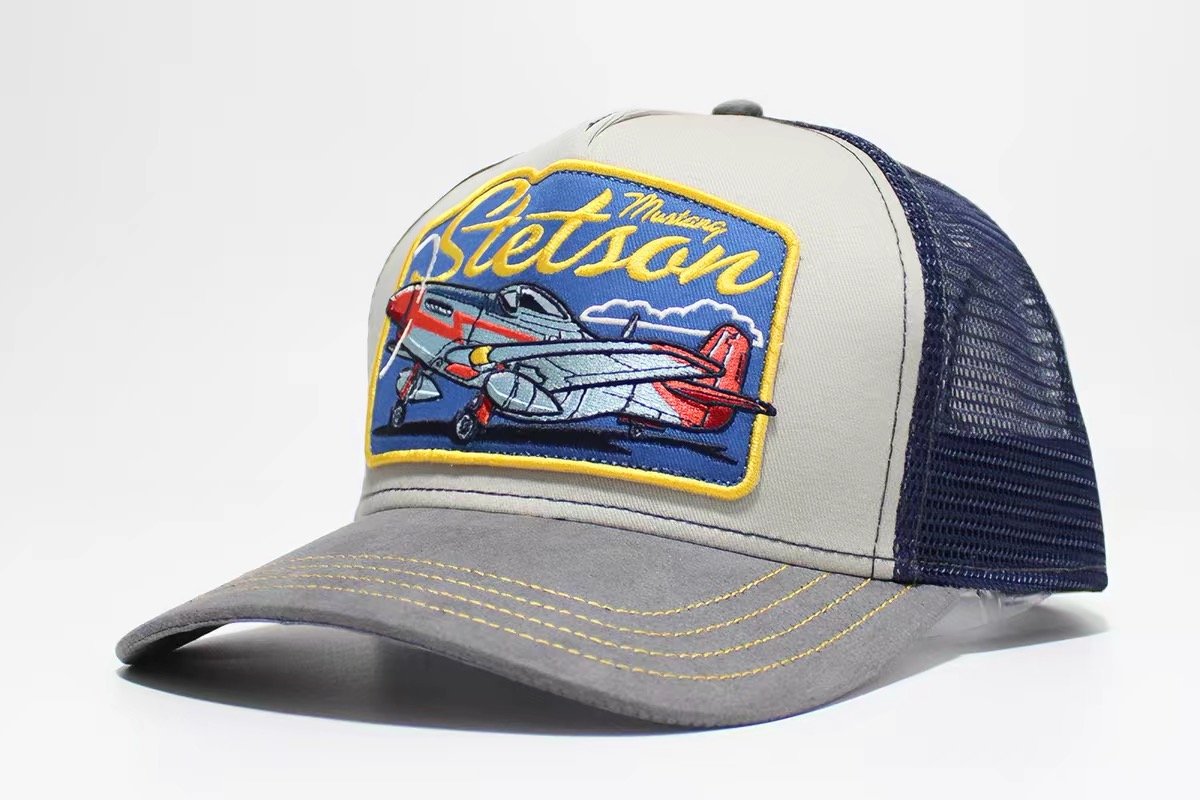 Cream and gray trucker hat with navy mesh and a yellow-bordered airplane patch