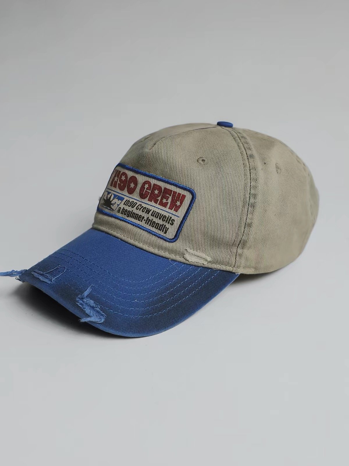 Khaki cap with a distressed blue curved brim and a rectangular front lettering patch