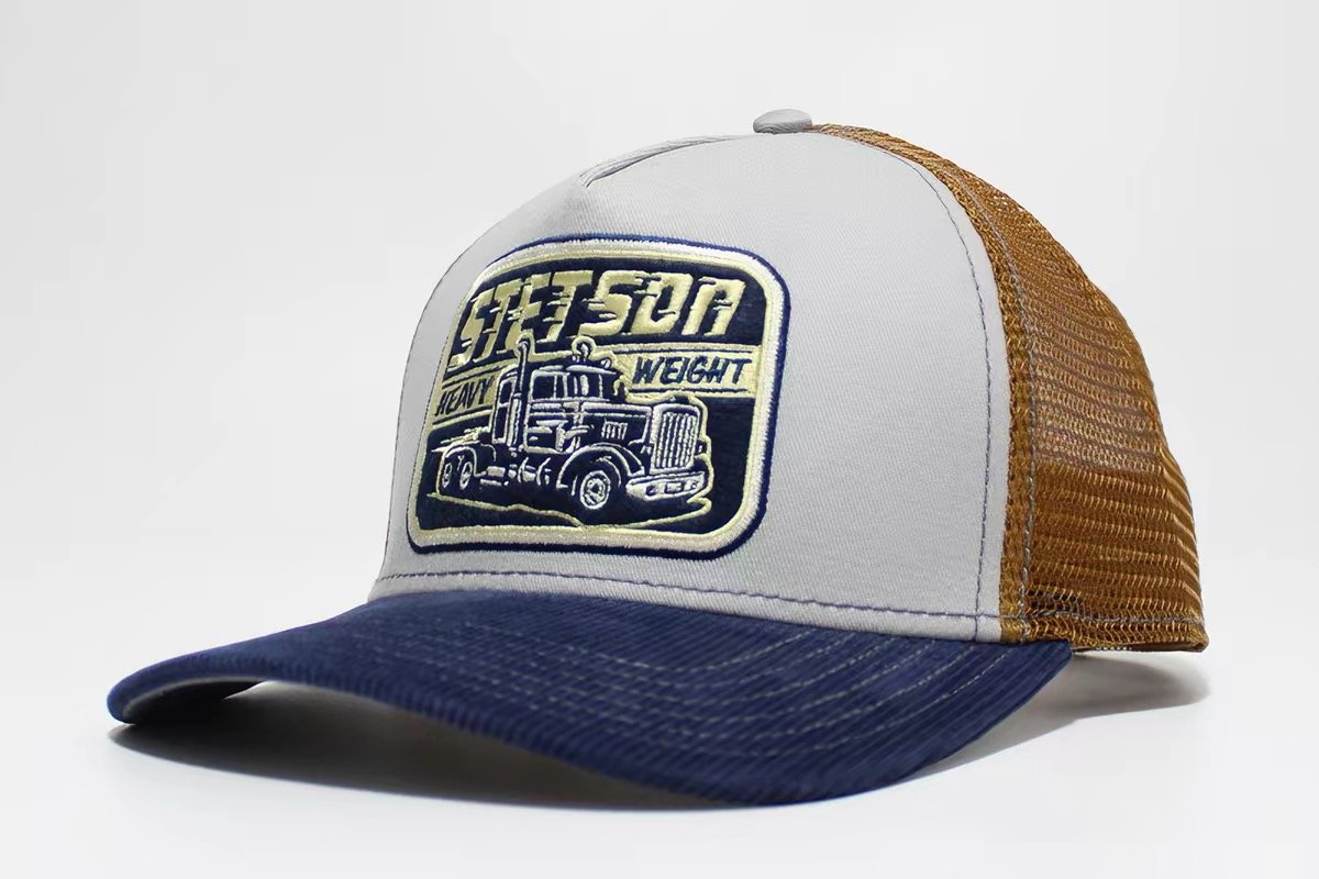 Light-front trucker hat with navy brim, ochre mesh and a truck illustration patch