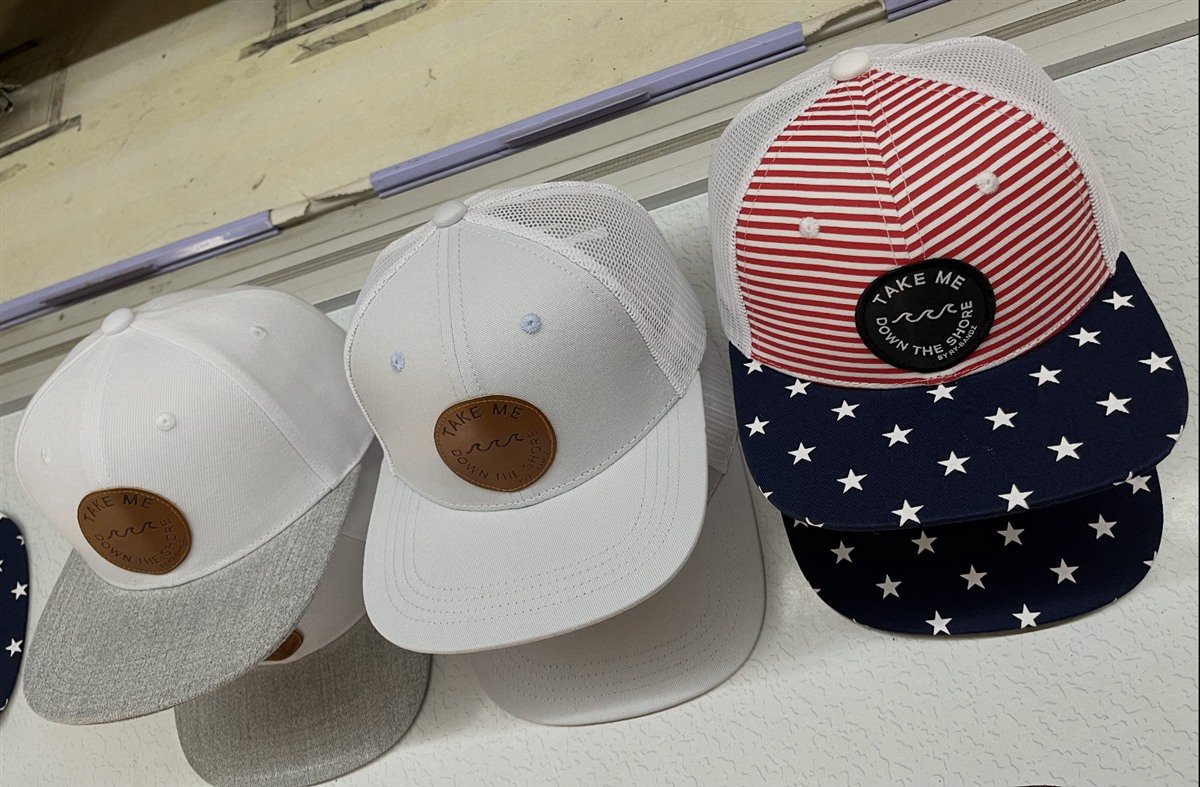 White caps with round brown leather patches, alongside a stars-and-stripes cap with a round black patch.