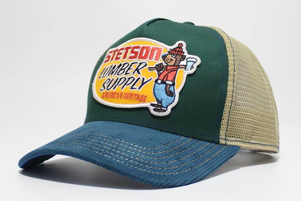 Green trucker hat with blue brim, beige mesh back and a shaped lumberjack patch