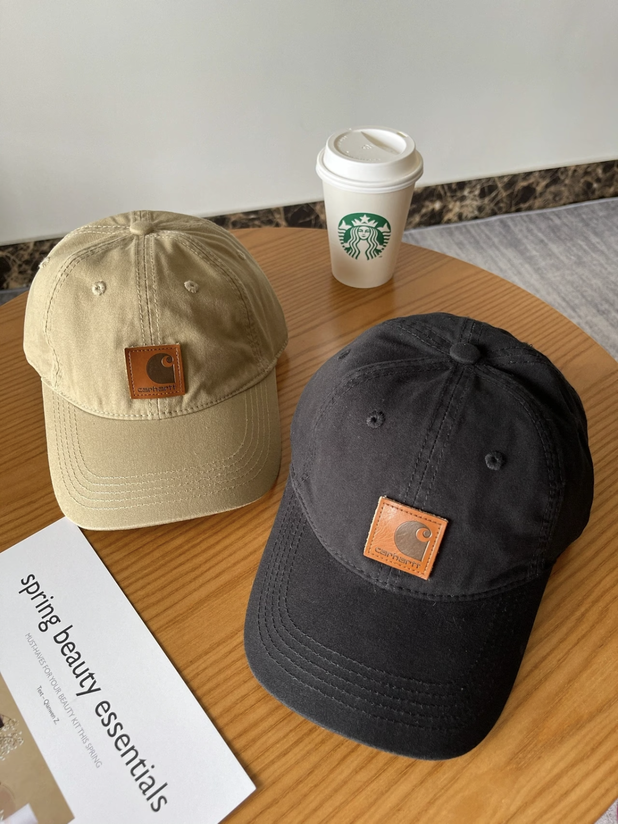 Khaki and black caps on a wooden table, each with a small square brown leather patch.