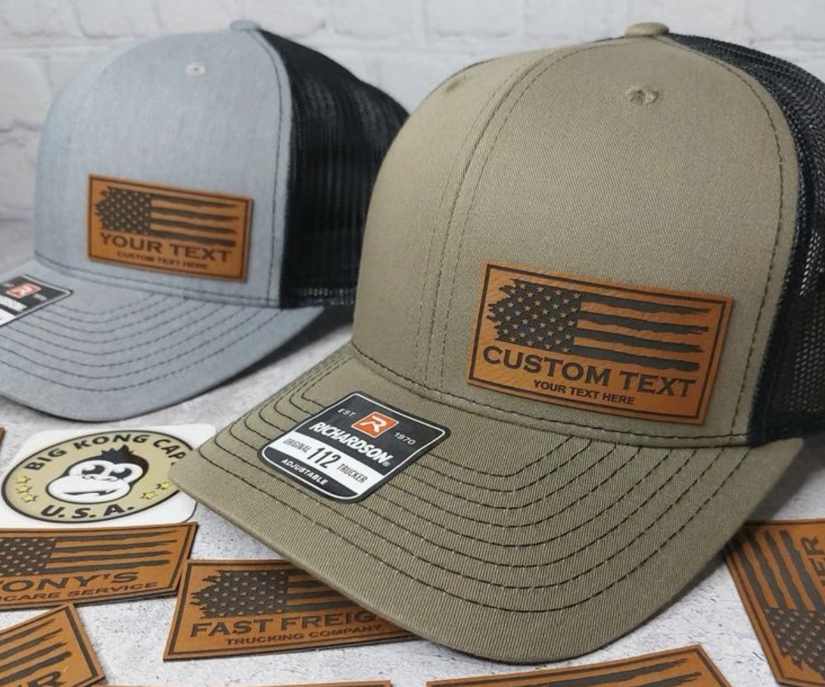 Custom leather patch hats in olive and gray with mesh backs and rectangular leather flag patches.