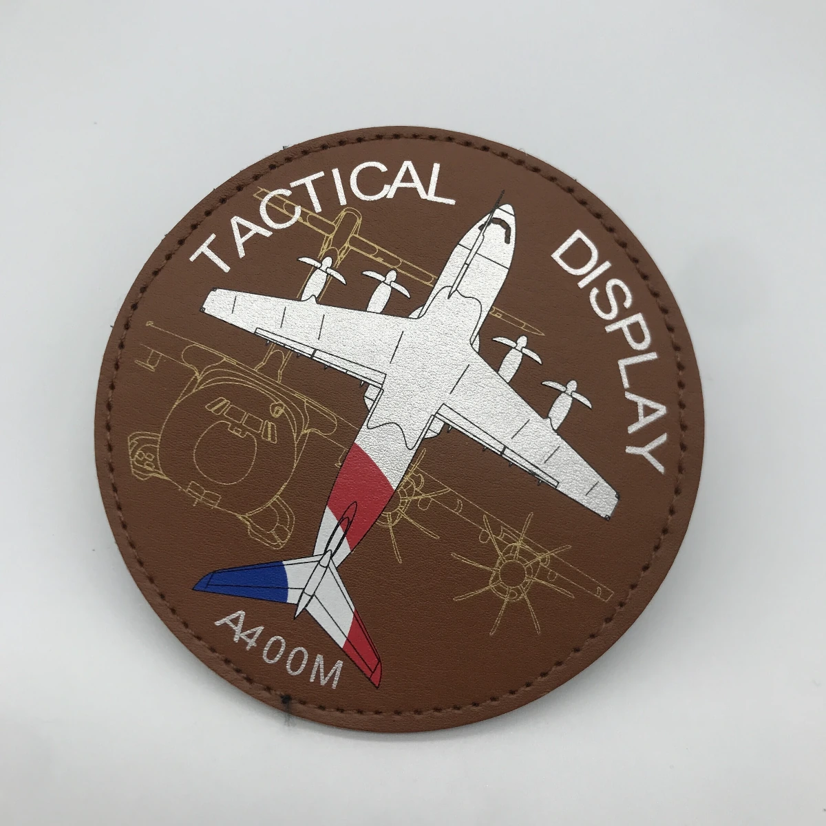 Round brown leather patch with a colored aircraft design, white lettering and stitched edge