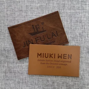 Two brown rectangular leather labels on grey woven fabric