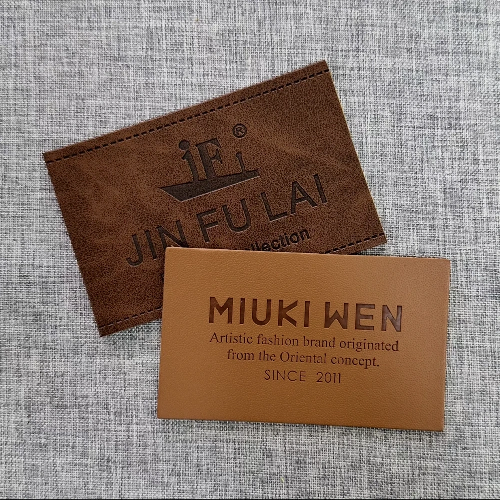 Two brown rectangular leather labels with dark lettering on grey woven fabric