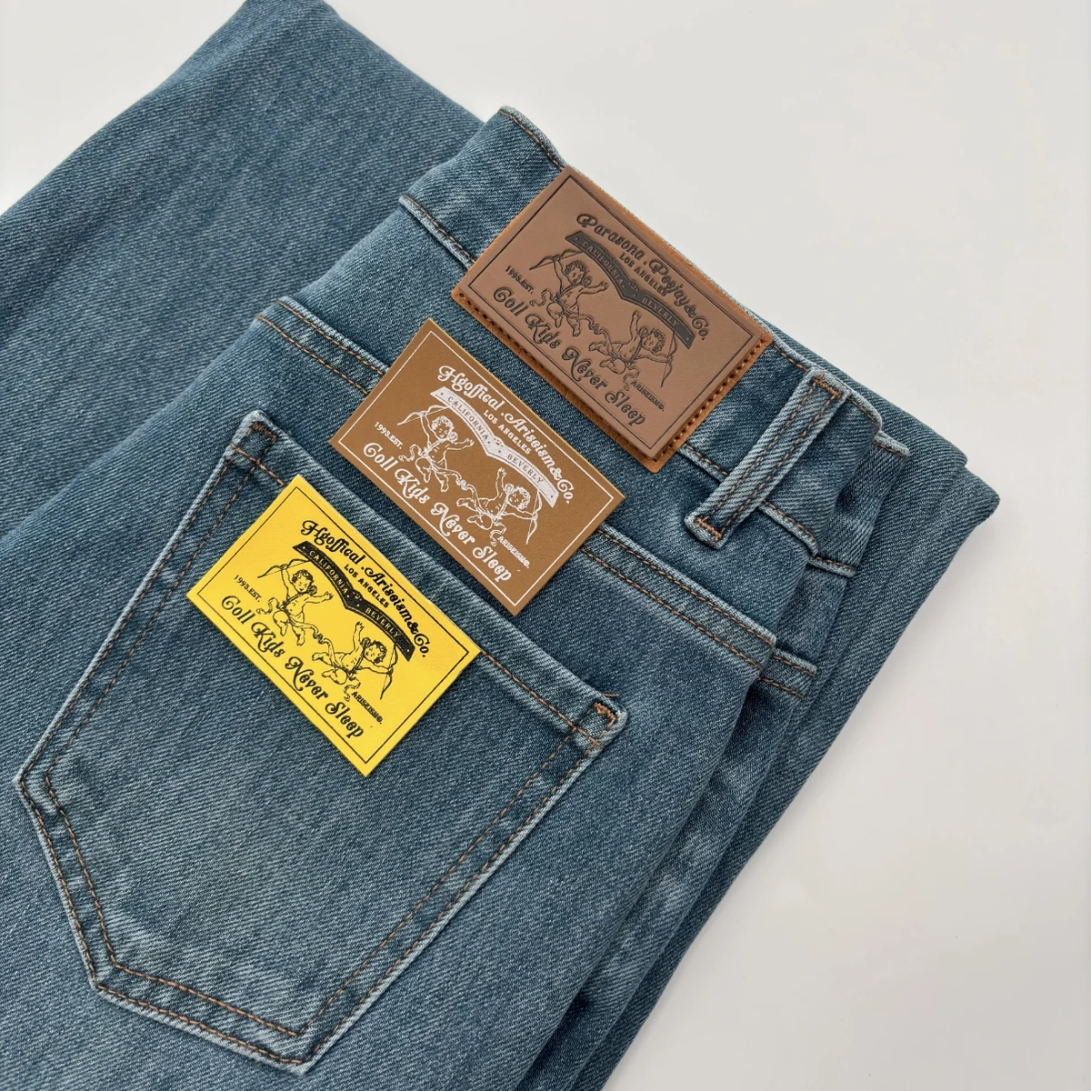 Three rectangular leather-look labels in brown, tan and yellow displayed on blue denim jeans