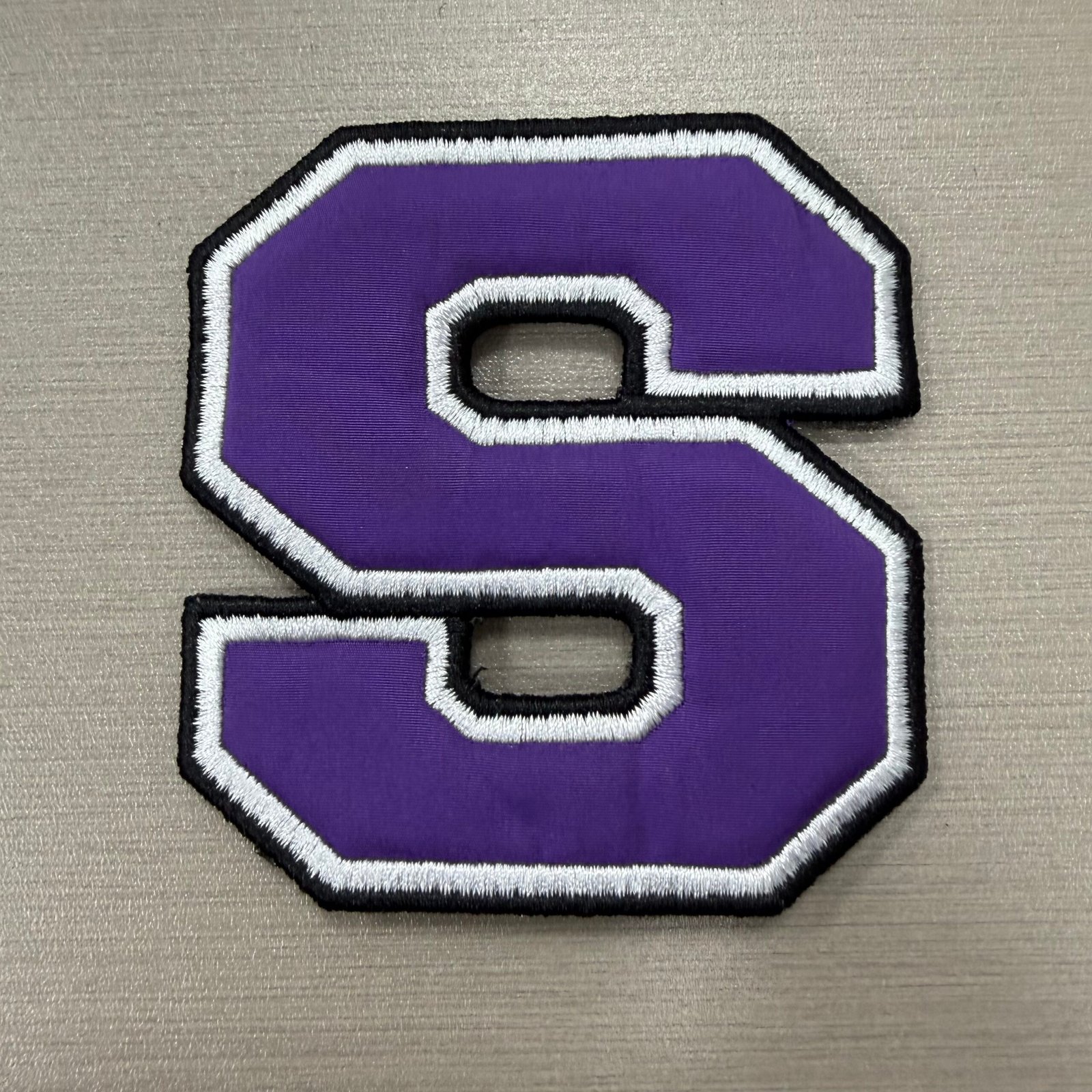 Purple S letter patch with white embroidered outline and black edge