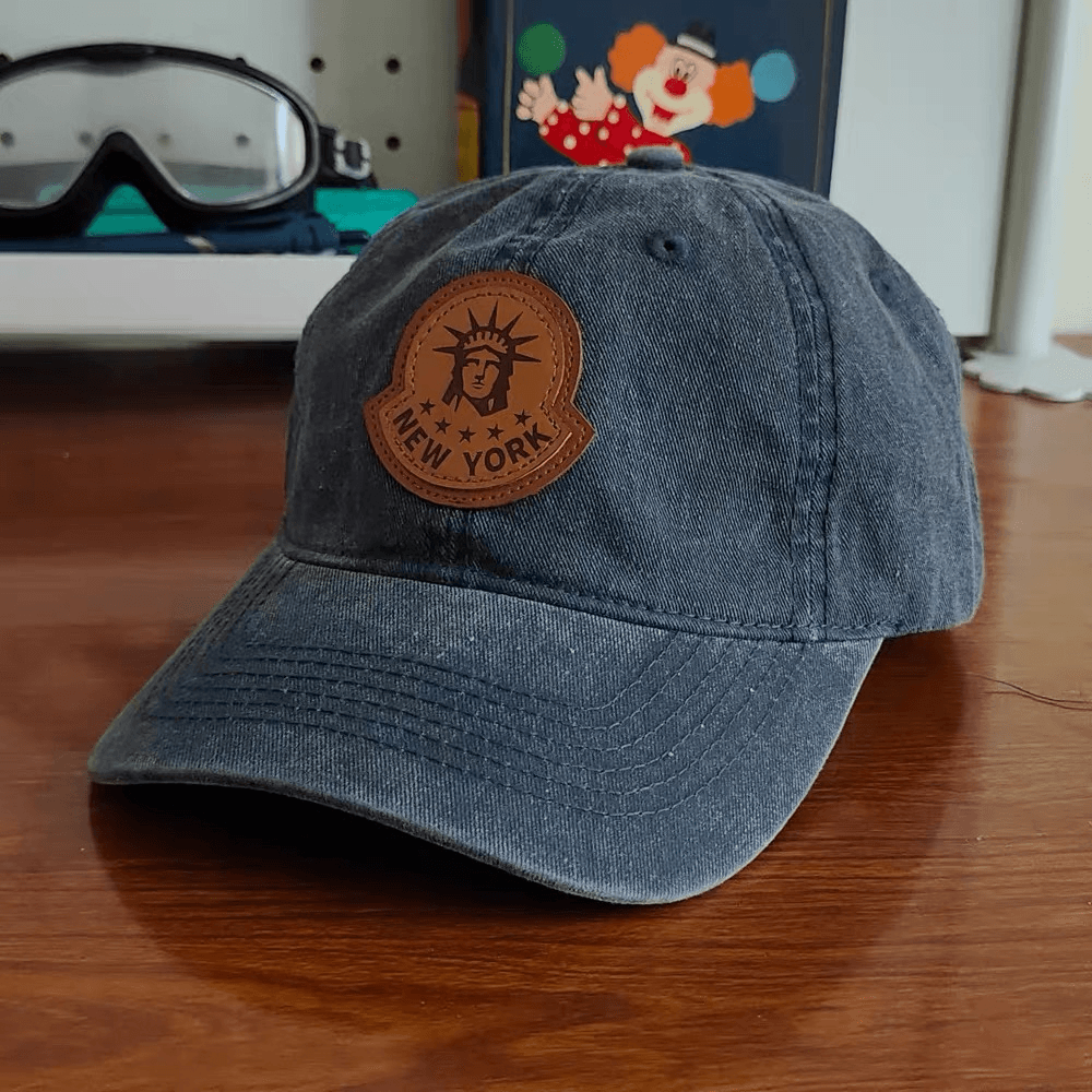 Washed navy cap with a shaped brown leather patch featuring a Statue of Liberty design.