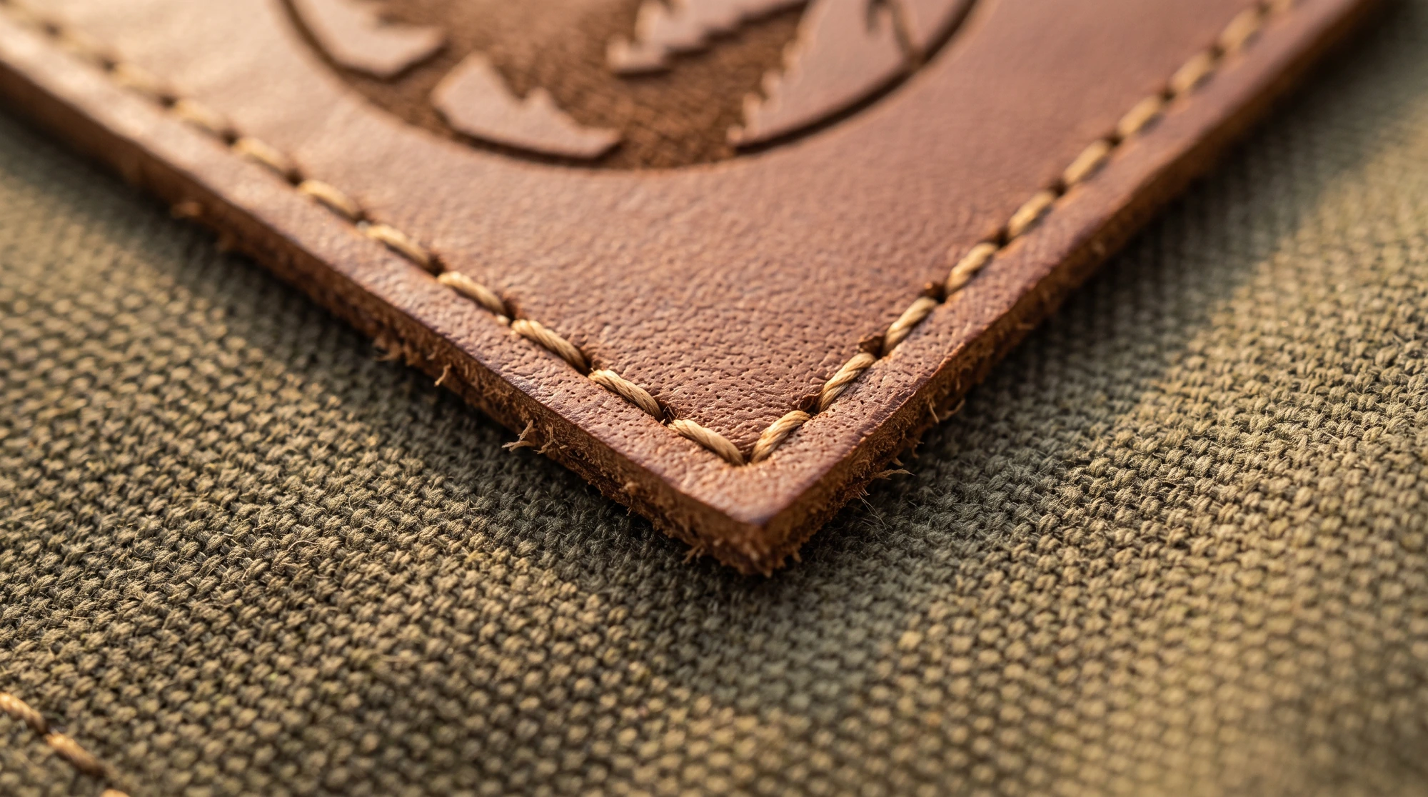 A brown leather patch sewn onto a canvas jacket with the stitch line about 3 mm inside the patch edge.